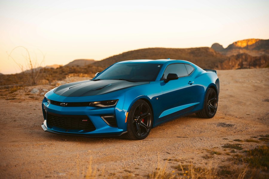 A blue car parked on a desert road at sunset